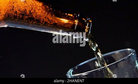 Gros plan du versement de la bière de la bouteille de verre brun dans le verre.Vidéo.Verser la boisson alcoolisée isolée sur fond noir, concept de fête Banque D'Images