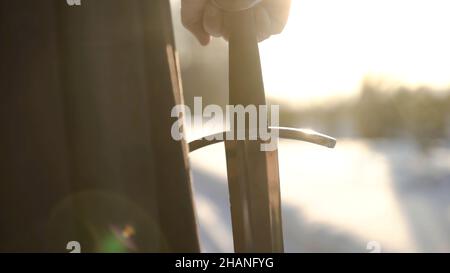 Homme en costume médiéval tenant une épée.Action.Gros plan de la main de l'homme dans un costume médiéval tenant une épée hilt sur fond de lumière du soleil.Vue épique de medieva Banque D'Images