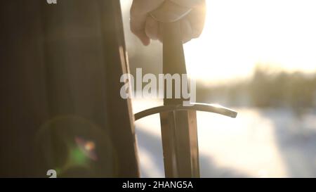 Homme en costume médiéval tenant une épée.Action.Gros plan de la main de l'homme dans un costume médiéval tenant une épée hilt sur fond de lumière du soleil.Vue épique de medieva Banque D'Images