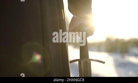 Homme en costume médiéval tenant une épée.Action.Gros plan de la main de l'homme dans un costume médiéval tenant une épée hilt sur fond de lumière du soleil.Vue épique de medieva Banque D'Images