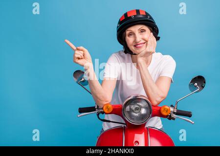 Photo portrait femme aînée assise sur un vélo portant un casque pointant l'espace vide isolé pastel bleu fond Banque D'Images