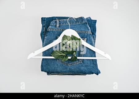 Mode durable, économie circulaire, vêtements écologiques en denim.Plante à feuilles vertes et porte-vêtements en bois sur fond bleu Jean denim Banque D'Images