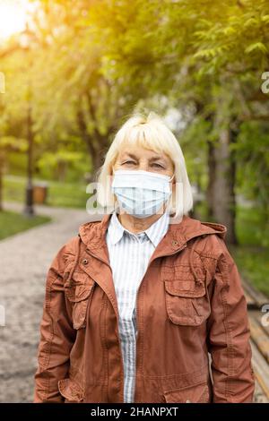 Une femme vaccinée avec un masque de protection contre le SRAS-COV-2 variante Omicron Covid-19, regarde la caméra dans un parc d'été de la ville.Bonjour printemps 2022 Banque D'Images
