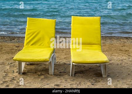 Une paire de chaises longues jaunes vides sur la plage de sable au bord de la mer Banque D'Images