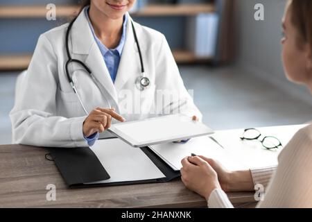 Jeune femme hindoue gaie médecin en manteau blanc avec stéthoscope montre le comprimé avec les résultats de l'examen dans la clinique de bureau Banque D'Images