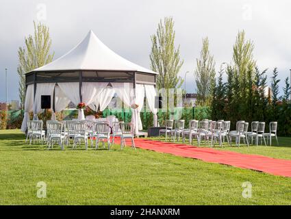 Chaises extérieures placées dans le jardin à côté de la moquette rouge et de la tente de mariée le jour du mariage Banque D'Images