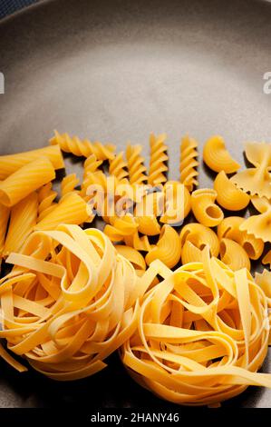 divers types de pâtes comme la fettuccine, le fusilli, le farfalle sur une assiette noire Banque D'Images