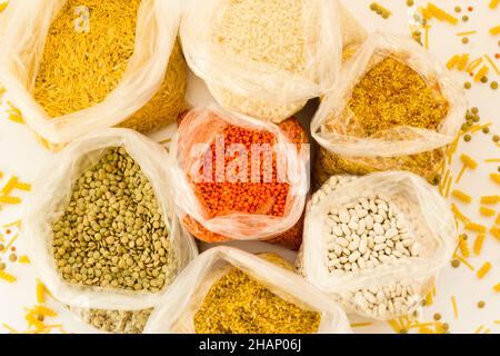 Groupe de céréales sèches non cuites dans des sacs en nylon sur la surface blanche, vue ci-dessus Banque D'Images