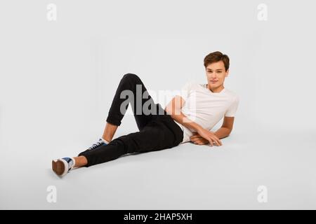 Beau t-shirt blanc, pantalon noir et baskets à moitié posé sur le sol sur fond gris.Tests de modèles Studio. Banque D'Images