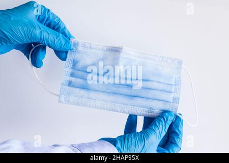 Main dans un gant en caoutchouc bleu tenant et contrôlant le fil du masque chirurgical à trois plis sur fond gris Banque D'Images