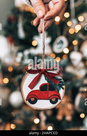 Main tenant ornement de noël en bois avec voiture rouge transportant l'arbre de noël Banque D'Images