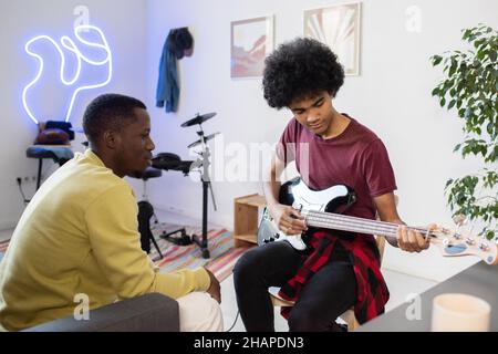 Professeur de musique de l'ethnie africaine consultant biracial gars avec guitare assis devant lui dans le milieu de la maison Banque D'Images