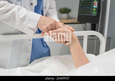Gros plan du médecin tenant la main de la patiente pendant qu'elle est allongée sur le lit à l'hôpital Banque D'Images
