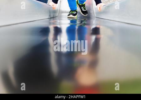 Vue partielle d'un enfant sur une aire de jeux, reflet sur une surface métallique. Banque D'Images