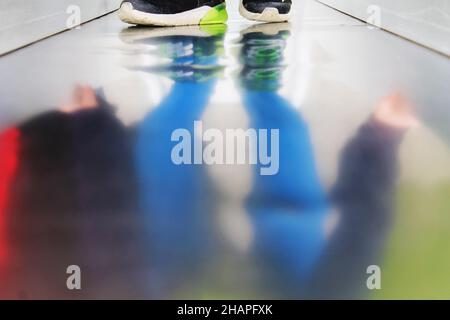 Vue partielle d'un enfant sur une aire de jeux, reflet sur une surface métallique. Banque D'Images