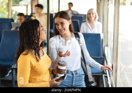 Belles femmes multiethniques souriantes debout dans le bus et parlant Banque D'Images