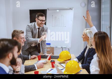Homme d'affaires souriant et réussi à parler de nouveau projet pendant que son équipe est assise à la salle de réunion et pose des questions.L'ambition est de mettre un Banque D'Images