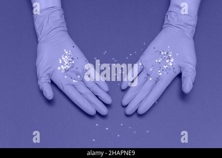 Mains dans des gants médicaux sur fond bleu. Petites étoiles scintillantes dans les mains. Concept de carte de Noël et de nouvel an. Vue de dessus photo, espace de copie. Banque D'Images