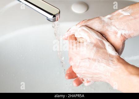 Se laver les mains avec du savon sous le robinet avec de l'eau dans la salle de bains pour protéger les germes du coronavirus.Gros plan des mains des hommes. Banque D'Images