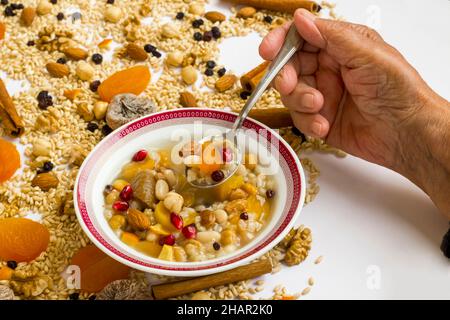 Une vieille main mange le dessert d'ahura dans un bol blanc sur les ingrédients du plat d'Ahure Banque D'Images