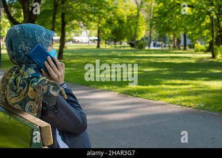 Profil de la femme enceinte musulmane portant un masque de visage parlant sur le smartphone Banque D'Images