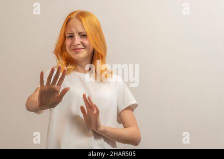 jeune fille avec des cheveux rouges dans un t-shirt blanc sur un fond clair mains avant dire non Banque D'Images