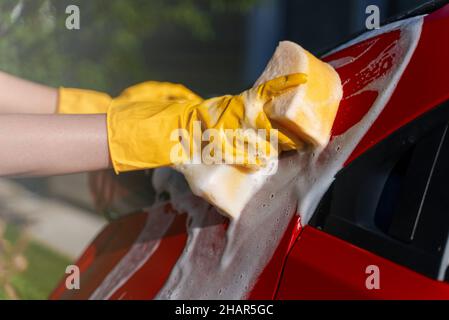 Femme en gants lave la voiture avec une éponge. Banque D'Images