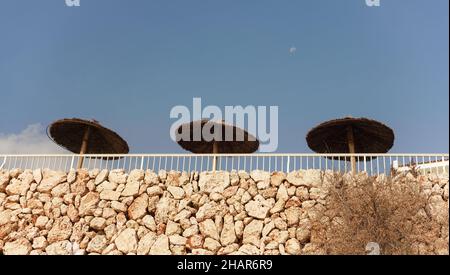 Vue sur le mur en pierre, parasols en paille près de la station de l'hôtel, ciel clair au-dessus Banque D'Images