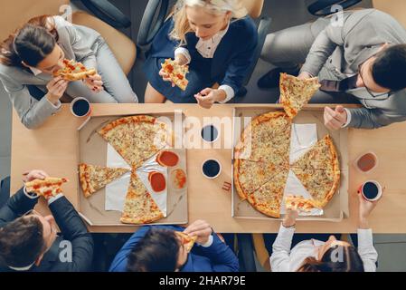 Vue de dessus des hommes d'affaires en tenue habillée assis à table et prenant une pizza pour le déjeuner. Banque D'Images