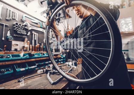 Homme dédié au Caucase qui pose un pneu sur la roue de vélo tout en étant debout dans l'atelier. Banque D'Images