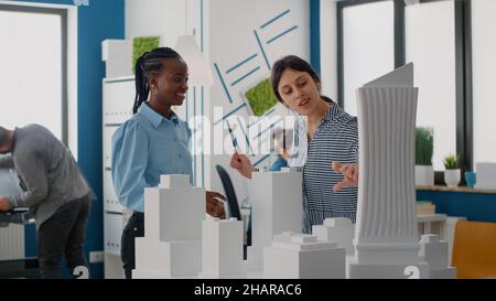 Les architectes donnent des cinq hauts et célèbrent les progrès du projet urbain avec le modèle de construction.Les employés travaillent en équipe sur la conception et la structure de la construction, en utilisant des règles de conduite au bureau. Banque D'Images