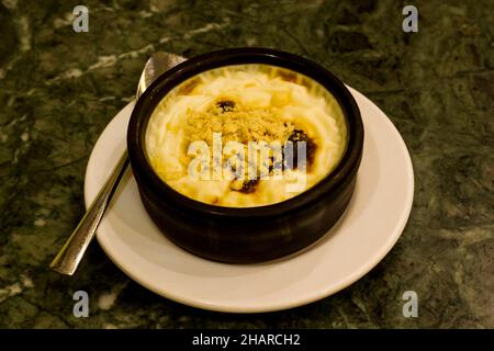 Pudding traditionnel de riz de style turc cuit dans une casserole, bols de dessert en argile sur la table en marbre de granit. Banque D'Images