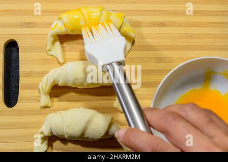Chef peignant de petits croissants savoureux avec du jaune d'œuf sur une planche de bois Banque D'Images