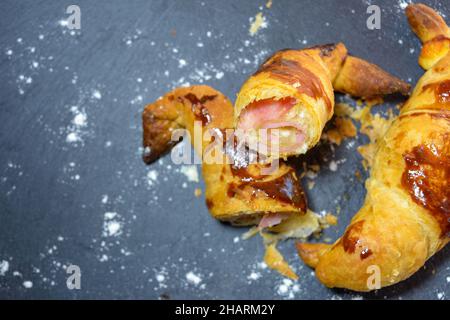 Croissants frais farcis au jambon et au fromage fondu, prêts à manger, sur une assiette en ardoise grise Banque D'Images