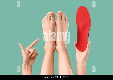 Femme avec une semelle intérieure orthopédique rouge pointant vers ses pieds sur fond vert Banque D'Images