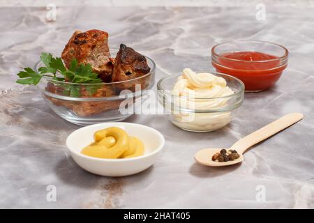 Porc grillé dans un bol en verre avec persil frais.Bols avec ketchup, sauce au fromage et moutarde. Banque D'Images