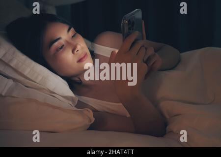 Une femme utilise le téléphone sur le lit avant de dormir la nuit. Banque D'Images