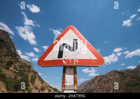 Le triangle de signalisation rouge et blanc standard pour une section curvy d'une route.Dans la région du réservoir du lac Charvak près de Tachkent, Ouzbékistan. Banque D'Images