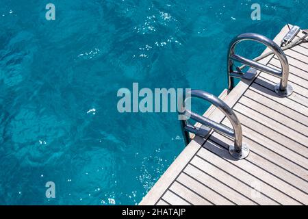 Pont arrière du bateau, échelles en bois de teck et en métal, fond bleu d'eau de mer.Croisière en yacht de luxe, mer Egée Grèce Banque D'Images