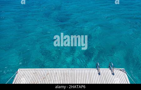 Pont arrière du bateau, échelles en bois de teck et en métal, fond bleu d'eau de mer.Croisière en yacht de luxe, mer Egée Grèce Banque D'Images