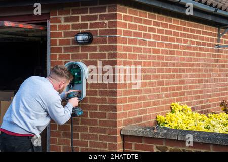 Électricien installant un chargeur de voiture électrique Zappi sur le mur extérieur d'un garage privé.NB: Les locaux dans la photographie sont la propriété libérée. Banque D'Images