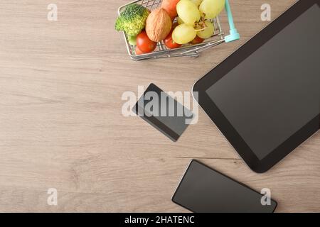 Concept d'achat en ligne avec appareils mobiles et mini supermarché panier plein de fruits et légumes sur table en bois.Vue de dessus.COM. Horizontale Banque D'Images