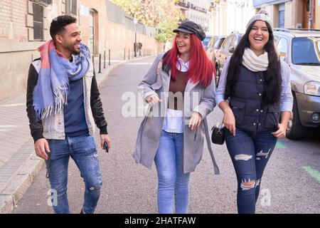 Corps complet d'amis multiethniques masculins et féminins dans un élégant vêtement décontracté marchant sur la route d'asphalte au-delà des voitures et ayant la conversation Banque D'Images