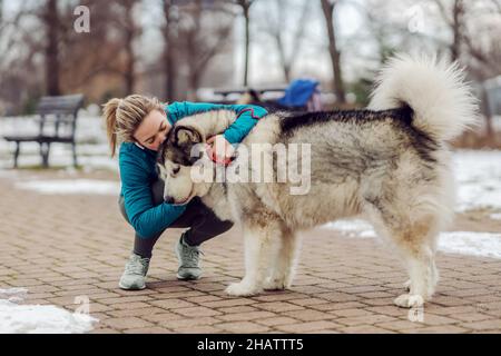 Sportswoman embrassant son chien et l'embrassant tout en se broutant dans le parc par temps neigeux.Animaux de compagnie, loisirs, activités de fin de semaine Banque D'Images