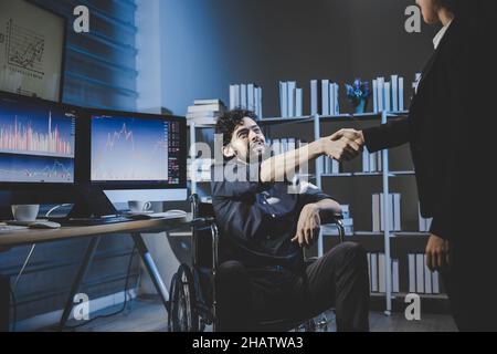 Un homme en fauteuil roulant se met à serrer la main et commence à travailler au bureau de nuit.Ses collègues sont passionnés par le travail. Banque D'Images