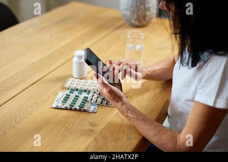 Femme âgée lisant les instructions de médicaments d'ordonnance en ligne, défilement par téléphone, médecin et consultation en ligne, femme âgée vérifie re Banque D'Images