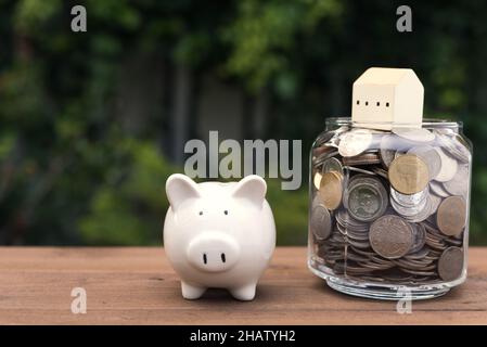 Piggy banque et modèle de maison sur pièces d'argent verre pot sur bois tabel, économie et investissement concept Banque D'Images