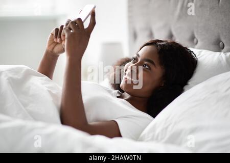 Gaie jeune femme noire discutant avec un petit ami au lit Banque D'Images