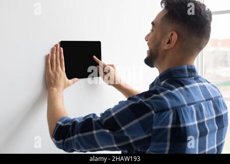 Homme heureux utilisant le système de contrôle de maison mural intelligent Banque D'Images