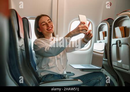 Jeune femme gaie faisant le selfie dans l'avion Banque D'Images